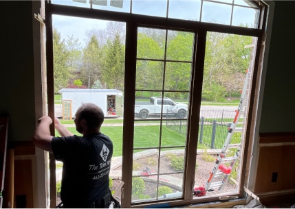 The Trim Wright craftsman installing a large wood framed window.